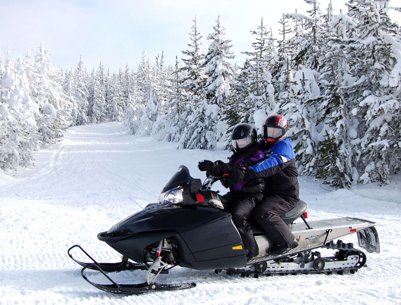 Two people on a snowmobile posing for a photo while parked on a snowy trail